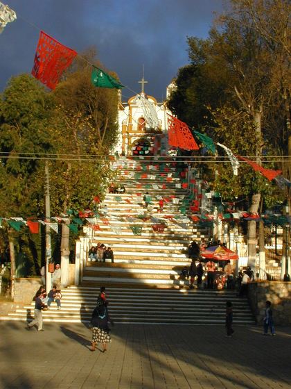 A village fiesta — flags, church steps and a market below